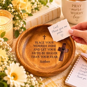 Puede incluir: Un cuenco de madera redondo con el texto grabado: PLACE YOUR WORRIES HERE AND LET YOUR FAITH BE BIGGER THAN YOUR FEAR. Amber. El cuenco incluye una pequeña cruz de madera y una nota de papel blanca con el texto: Lord, Please give me peace.