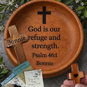 May include: A round wooden bowl with a dark brown cross and the engraved text God is our refuge and strength. Psalm 46:1 Bonnie. Included are two small wooden crosses, one with a heart cutout, and two printed cards with religious text.