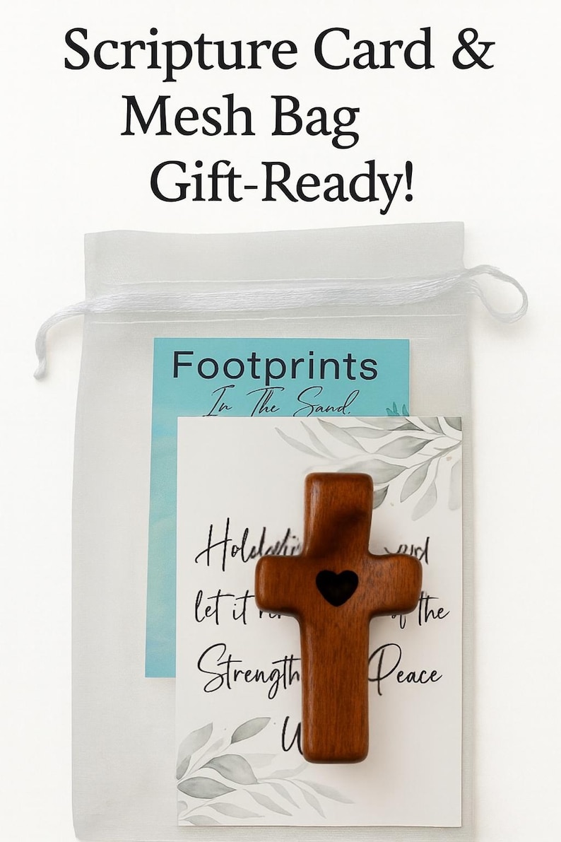 May include: A gift-ready mesh bag containing a wooden cross with a heart cutout, and two cards. The cards have the text "Footprints In The Sand" and a scripture about strength and peace. The bag is white.