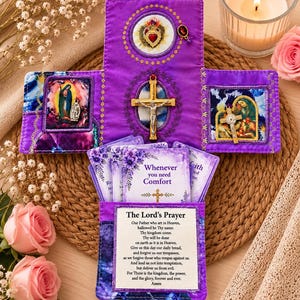 May include: A purple fabric devotional case featuring a central gold crucifix, a Sacred Heart emblem, and two religious images. The case holds a deck of cards, with the front card displaying the text The Lord's Prayer and another card reading Whenever you need Comfort.