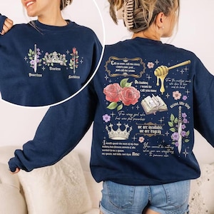 May include: Navy blue sweatshirt with floral and crown graphics. The front features a sword, crown, and flower design with the words "Powerless," "Fearless," and "Reckless." The back has roses, a book, and text.