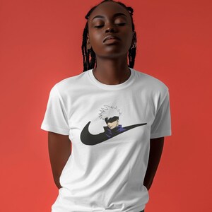 May include: White t-shirt with a black Nike swoosh logo and a cartoon character with white hair and a black eye patch. The character is wearing a purple shirt and is positioned inside the swoosh.