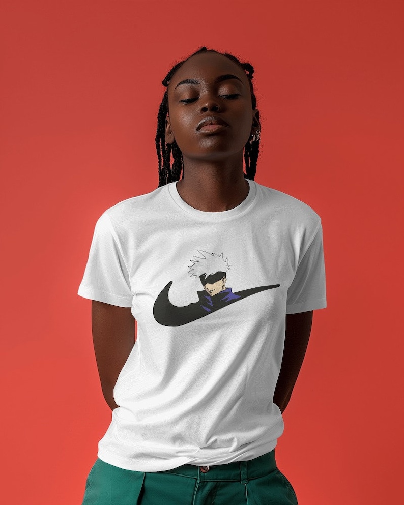 May include: White t-shirt with a black Nike swoosh logo and a cartoon character with white hair and a black eye patch. The character is wearing a purple shirt and is positioned inside the swoosh.