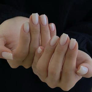 May include: Close-up of hands with short, square-shaped nails painted a light, creamy white.