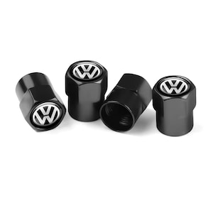 Puede incluir: Juego de cuatro tapones de válvula de neumático negros hexagonales con un logotipo blanco de Volkswagen. Los tapones tienen un acabado brillante. El logotipo de Volkswagen está centrado en la parte superior de cada tapón.