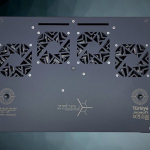May include: A black metal box with three square cutouts featuring a geometric pattern. The box has the text "zebay cooler" and "T&uuml;rkiye Jeosoft" printed on it. The text "Model No: ZC-HLMNR SN: HLMR-H8570  Input: 12V - 3A  (PATENT PENDING)" is also printed on the box.