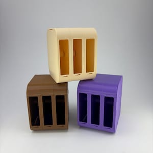 Op de afbeelding: Drie 3D-geprinte opbergcontainers in beige, bruin en paars. Elke container heeft drie rechthoekige openingen. De containers zijn op elkaar gestapeld tegen een witte achtergrond. De containers hebben afgeronde randen.