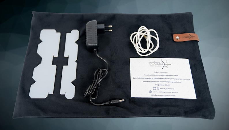 May include: A black velvet pouch with a brown leather tag that says "zelbou" contains a white light panel, a black power adapter, a white cable, and a white instruction sheet with the text "zelbou" and contact information.