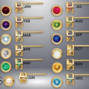 May include: A collection of gold-colored stud earrings, each featuring a different gemstone and corresponding month label. The gemstones include red, purple, blue, white, green, yellow, and pearl. The earrings are displayed on a gradient gray background.