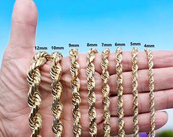 Può includere: Primo piano di una mano che tiene nove catene a corda d'oro di diverse dimensioni, che vanno da 4 mm a 12 mm di diametro. Le catene sono disposte in ordine di dimensione, con la catena più piccola a destra e la catena più grande a sinistra. Le catene sono tutte in oro massiccio e hanno una finitura lucida.