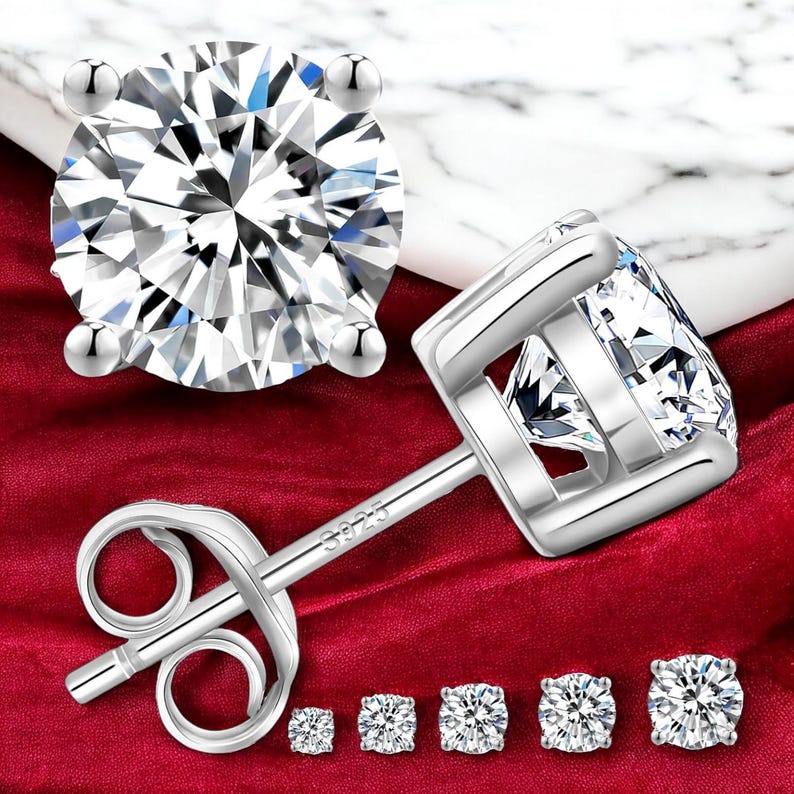 May include: A set of six silver stud earrings with clear cubic zirconia stones. The earrings are shown on a red velvet background. The earrings are available in different sizes.