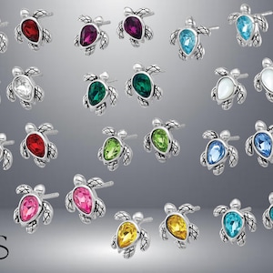 May include: A set of 18 pairs of silver turtle earrings with various colored crystal accents. The earrings are arranged in rows of three, with each row featuring a different color of crystal.