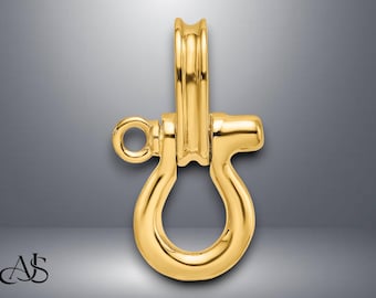 Pode incluir: Um pingente de manilha dourado com formato em U arredondado e uma argola circular em um lado. O pingente tem uma superfície lisa e polida e uma pequena barra retangular na parte superior. O fundo é um gradiente de cinza.