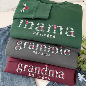 May include: Three sweatshirts in different colours with floral embroidery spelling out "mama", "grammie", and "grandma" with the year "EST. 2025" underneath each word.