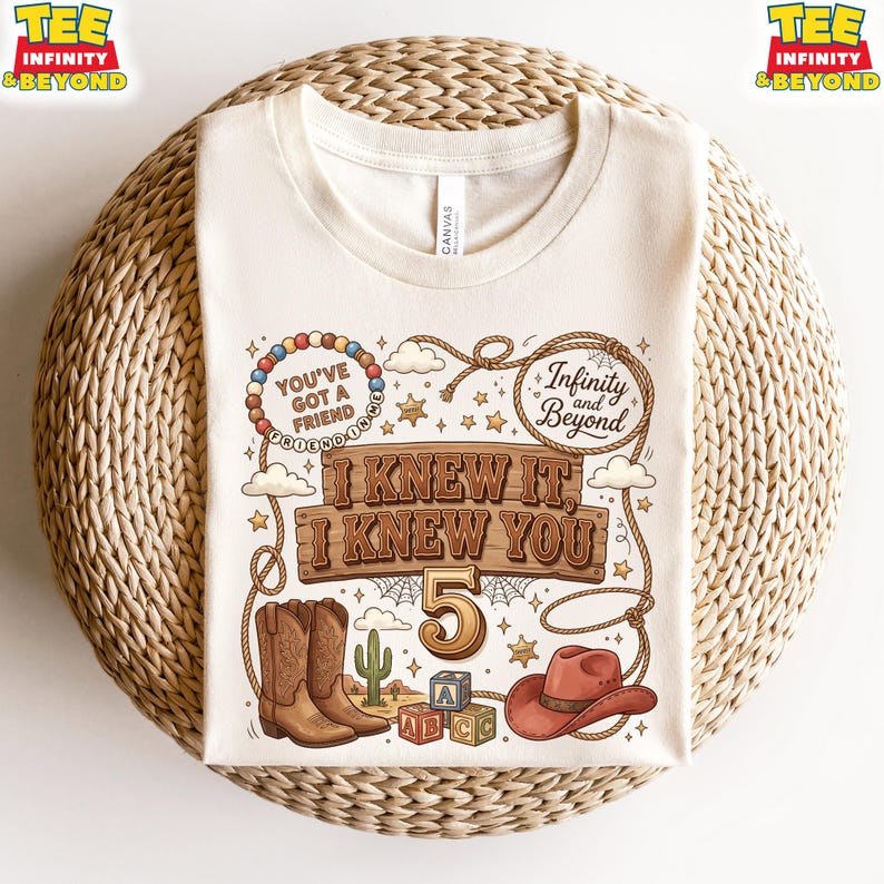 May include: A cream-colored t-shirt featuring a graphic print with a lasso, cowboy boots, a cowboy hat, alphabet blocks, and a cactus. The text reads: You've Got A Friend In Me, Infinity and Beyond, and I Knew It, I Knew You, with the number 5.