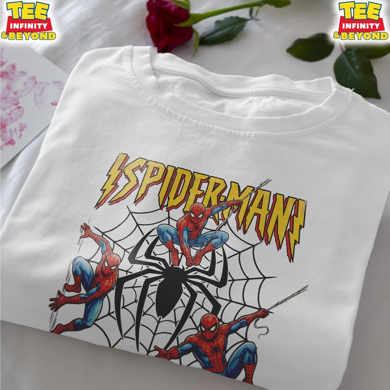 May include: White t-shirt featuring a graphic of Spider-Man and a spider web design. The text "SPIDERMAN" is in yellow with a lightning bolt design. Three Spider-Man figures are in action poses.