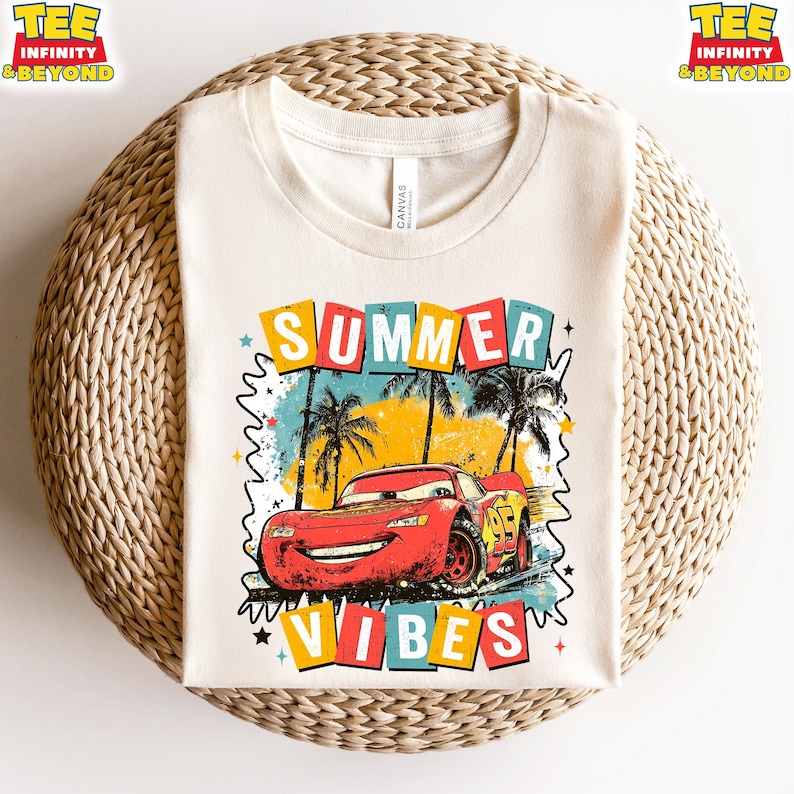 May include: Cream-colored t-shirt featuring a graphic of a red race car with the text "SUMMER VIBES". The design includes palm trees, colorful squares, and stars, evoking a summer theme. The shirt is made of a soft material.