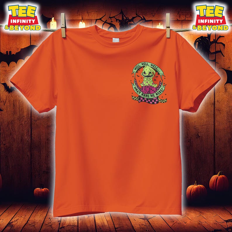 May include: Orange t-shirt with a graphic of a green character inside a crescent moon, with the text "WELL WELL WELL... WHAT HAVE WE HERE?" in a circular design. The shirt is hanging on a clothesline with a Halloween theme.