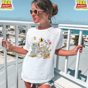 Puede incluir: Camiseta blanca con un gr&aacute;fico colorido de animales de dibujos animados celebrando un cumplea&ntilde;os. El gr&aacute;fico incluye una estrella con el n&uacute;mero 3, globos y el nombre "Flame". La camiseta tiene el texto "TEE INFINITY & BEYOND" en la parte superior.