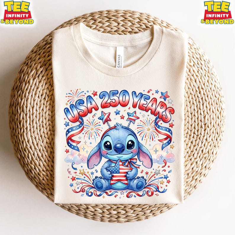 May include: Cream-colored t-shirt featuring a cartoon Stitch character holding a star-shaped American flag. The shirt has the text "USA 250 YEARS" in red, white, and blue, with fireworks and star accents. The shirt is displayed on a woven surface.