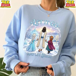 以下が含まれることがあります： 雪景色の中を2人の子供と歩くイエスのグラフィックが特徴の、水色のスウェットシャツ。「LET IT GO」と「AND LET JESUS」の文字が前面にプリントされています。スウェットシャツは長袖で、クルーネックです。