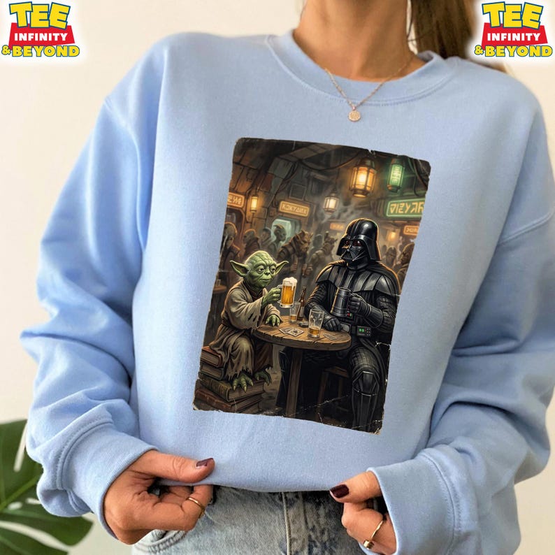 K&ouml;nnte beinhalten: Hellblaues Sweatshirt mit einer Grafik von Yoda und Darth Vader in einer Bar, beide mit Bier. Das Bild hat einen Vintage-Illustrationsstil. Auf dem Sweatshirt stehen die Worte "TEE INFINITY & BEYOND" oben links und rechts.