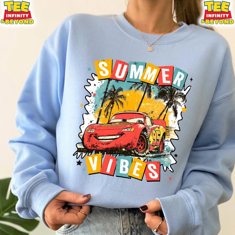 May include: Light blue sweatshirt featuring a graphic of a red race car with the number 95, palm trees, and the words "SUMMER VIBES" in colorful block letters. The sweatshirt has long sleeves and a crew neck.
