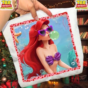 May include: White pillow with a colorful graphic of a mermaid wearing heart-shaped sunglasses and blowing a bubble. The mermaid has red hair and a purple seashell top. The pillow has a pink and red border and the text "TEE INFINITY & BEYOND".