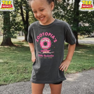 Puede incluir: Camiseta gris oscuro con el texto "ZOOTOPIA'S THE BIG DONUT" y un gr&aacute;fico de donut rosa. Debajo del donut est&aacute; el texto "Little Rodentia" y las palabras "DONUTS - BAGEL - SCOFFEE". La camiseta tiene el logo "TEE INFINITY & BEYOND".
