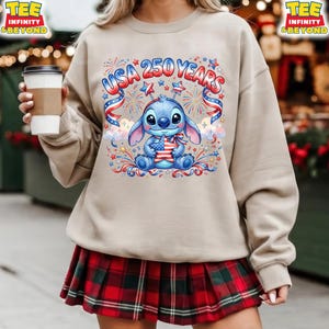 May include: Beige sweatshirt with a graphic of a blue cartoon character holding a star-shaped American flag, with the text "USA 250 YEARS" above. The design includes red, white, and blue fireworks and ribbons. The person is wearing a red and green plaid skirt.