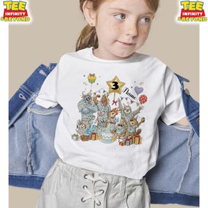 Puede incluir: Camiseta blanca con un gr&aacute;fico colorido de animales de dibujos animados celebrando un cumplea&ntilde;os. El n&uacute;mero "3" se muestra en una estrella, con la palabra "Name" debajo. Tambi&eacute;n se muestran globos, regalos y una tarta.