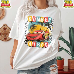 May include: White t-shirt featuring a graphic of a red race car with the text "SUMMER VIBES". The design includes palm trees and a colorful background. The shirt has short sleeves and a relaxed fit.