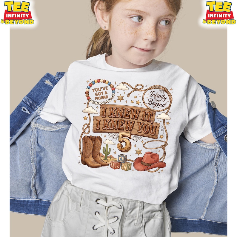 May include: A white t-shirt featuring a western-themed graphic with brown cowboy boots, a red cowboy hat, alphabet blocks, a cactus, and a lasso. The text reads: You've Got A Friend, Infinity and Beyond, I Knew It, I Knew You, and the number 5.