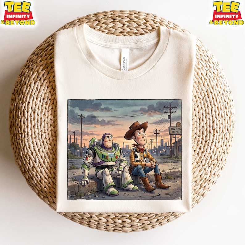 May include: Off-white t-shirt with a colourful illustration of Buzz Lightyear and Woody from Toy Story. The characters are sitting on a kerb with a cityscape background. The shirt has the text "TEE INFINITY & BEYOND".