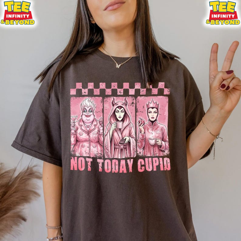 May include: Dark brown t-shirt featuring a pink graphic with three cartoon villains. The graphic includes the text "NOT TODAY CUPID" in pink. The shirt has a crew neck and short sleeves.