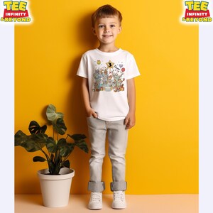 Puede incluir: Un ni&ntilde;o lleva una camiseta blanca con un gr&aacute;fico de dibujos animados de animales, globos y una tarta de cumplea&ntilde;os. El n&uacute;mero "3" est&aacute; en una estrella. El ni&ntilde;o lleva pantalones grises y zapatillas blancas. El fondo es amarillo.