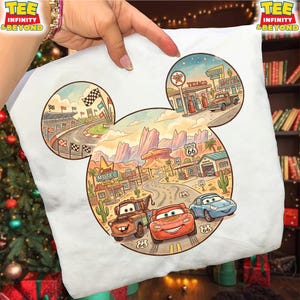 May include: White t-shirt featuring a colorful illustration of a race track, a desert landscape with Route 66, and cartoon cars. The design is shaped like Mickey Mouse's head. The shirt has the text "TEE INFINITY & BEYOND".
