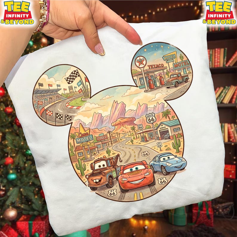 May include: White t-shirt featuring a colorful illustration of a race track, a desert landscape with Route 66, and cartoon cars. The design is shaped like Mickey Mouse's head. The shirt has the text "TEE INFINITY & BEYOND".