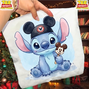 K&ouml;nnte beinhalten: Wei&szlig;es Kissen mit einer blauen Cartoonfigur, die einen schwarzen Hut mit dem Text "Magic Park Adventure" tr&auml;gt. Die Figur h&auml;lt einen Mickey Mouse Eis am Stiel. Das Kissen hat einen hellblauen Aquarellhintergrund.