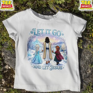 以下が含まれることがあります： 「LET IT GO」と「AND LET JESUS」の文字が入った白いTシャツ。イエスと2人の少女が雪景色の中にいるイラストが描かれています。