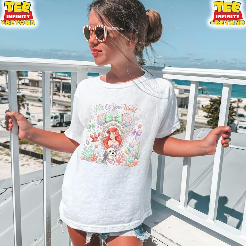 May include: White t-shirt featuring a colorful illustration of Ariel from The Little Mermaid, surrounded by sea creatures and the text "Part of Your World". The shirt has a crew neck and short sleeves.