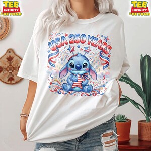 May include: White t-shirt featuring a blue cartoon character holding a star-shaped American flag. The shirt has the text "USA 250 YEARS" with red, white, and blue accents, fireworks, and stars, celebrating the United States.
