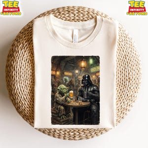 K&ouml;nnte beinhalten: Cremefarbenes T-Shirt mit einem Star Wars-Motiv. Die Grafik zeigt Yoda und Darth Vader in einer Bar, die Bier trinken. Das T-Shirt hat oben den Text "TEE INFINITY & BEYOND".