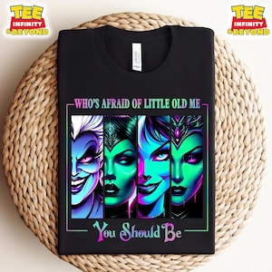 May include: Black t-shirt featuring a graphic of four villainous characters with vibrant colors. The text "WHO'S AFRAID OF LITTLE OLD ME" and "You Should Be" are displayed in a neon-style font, creating a bold statement.