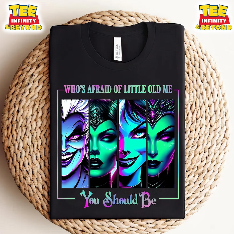 May include: Black t-shirt featuring a graphic of four villainous characters with vibrant colors. The text "WHO'S AFRAID OF LITTLE OLD ME" and "You Should Be" are displayed in a neon-style font, creating a bold statement.