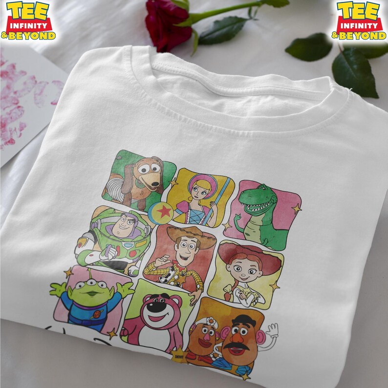 Puede incluir: Camiseta blanca con un gr&aacute;fico colorido de varios personajes de Toy Story, incluyendo a Buzz Lightyear y Woody. El dise&ntilde;o presenta m&uacute;ltiples personajes en una cuadr&iacute;cula. La camiseta tiene el texto "TEE INFINITY & BEYOND" en la parte superior.