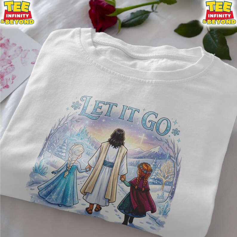 以下が含まれることがあります： 白いTシャツ。青い文字で「LET IT GO」と書かれています。グラフィックは、雪景色の中を歩く3人の人物（2人の女の子と1人の男性）を描いており、背景には城と山があります。