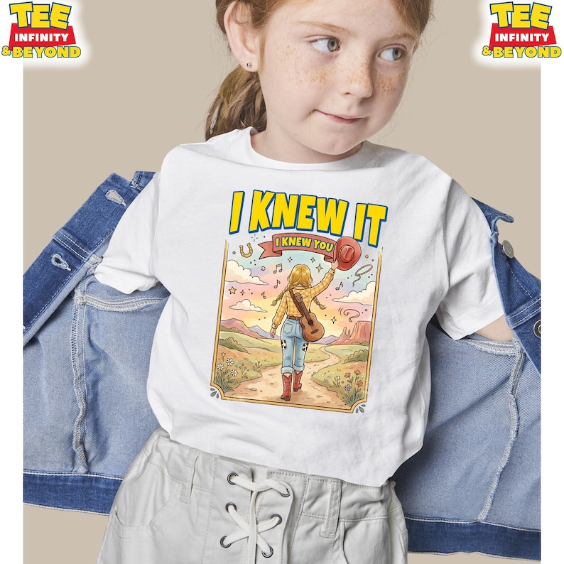 Puede incluir: Una camiseta blanca con una ilustraci&oacute;n gr&aacute;fica de una persona con trenzas rubias, vistiendo una camisa de cuadros amarilla, vaqueros azules y botas vaqueras rojas, caminando por un sendero con una guitarra y un sombrero rojo, con el texto I KNEW IT.