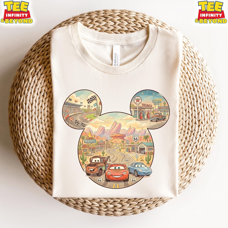 May include: Cream-colored t-shirt featuring a colorful graphic of the Cars movie characters in a Mickey Mouse head shape. The design includes race tracks, desert landscapes, and Route 66 elements. The shirt has the text "TEE INFINITY & BEYOND".