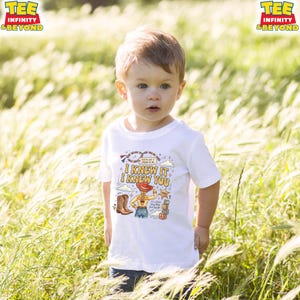 May include: A white short-sleeved t-shirt featuring a graphic print of a cowgirl character, cowboy boots, alphabet blocks, and the text "I KNEW IT I KNEW YOU" along with "YOU'VE GOT A FRIEND IN ME" and "It's a Jessie Story Baby Just Say Yes".
